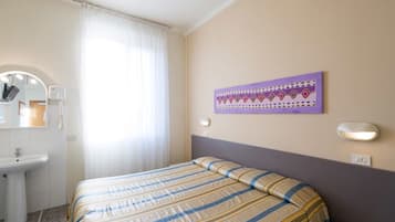 Une chambre d’hôtel comprenant un lit, une salle de bain avec un lavabo et un miroir, une fenêtre avec des rideaux et un luminaire fixé au mur.