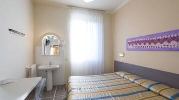 Una habitación de hotel con cama, baño con lavamanos y espejo, y ventana con cortinas.