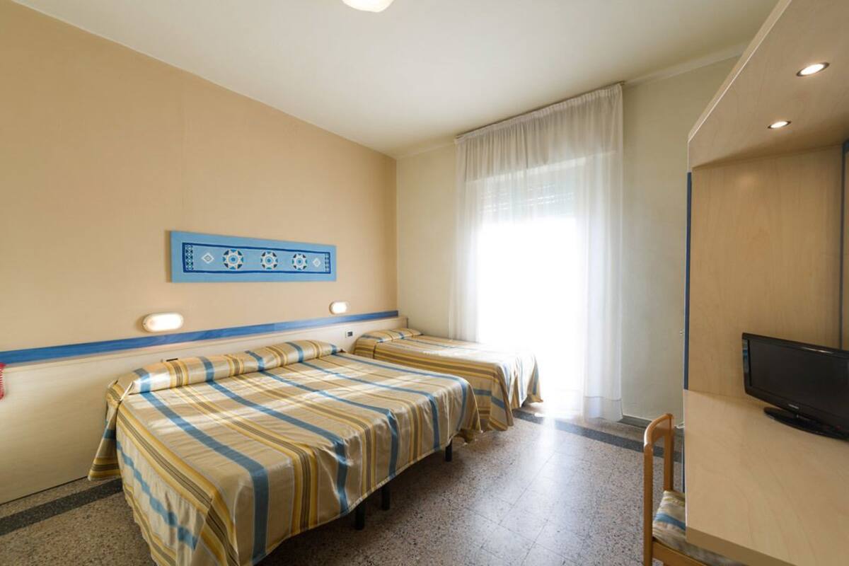 Una habitación de hotel con dos camas, televisión y ventana con cortinas.