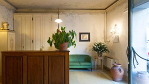 A room with a wooden cabinet, a green sofa, and potted plants. - Hotel Moderno (Pisa)