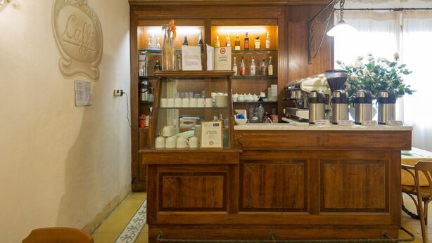 A bar area with wooden cabinets, shelves with bottles, and a coffee machine. - Hotel Moderno (Pisa)