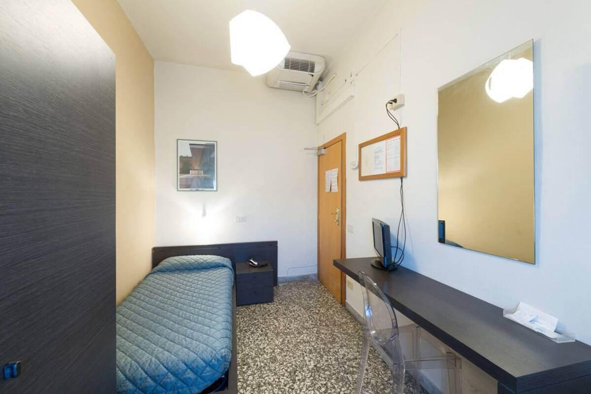 Habitación de hotel con cama, escritorio, espejo y aire acondicionado.