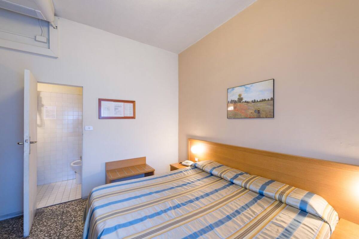 Una habitación de hotel con una cama, una mesita de noche y un cuadro en la pared.