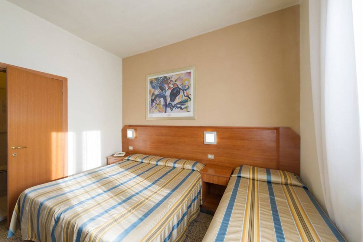 Habitación de hotel con dos camas individuales, cabecera de madera, un cuadro en la pared y una puerta a la izquierda.