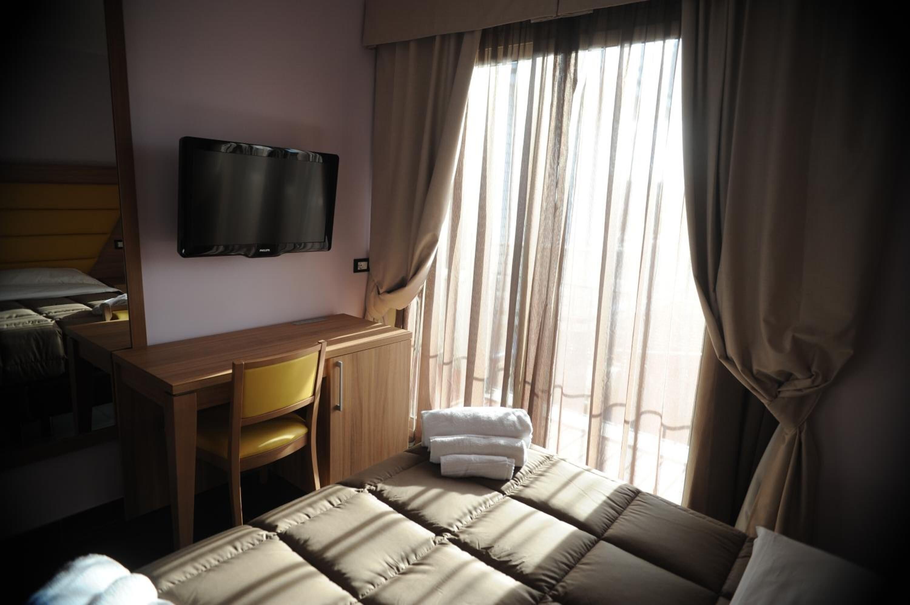 Une chambre d’hôtel équipée d’un lit, d’un bureau, d’une chaise, d’une télévision et d’une fenêtre avec des rideaux.