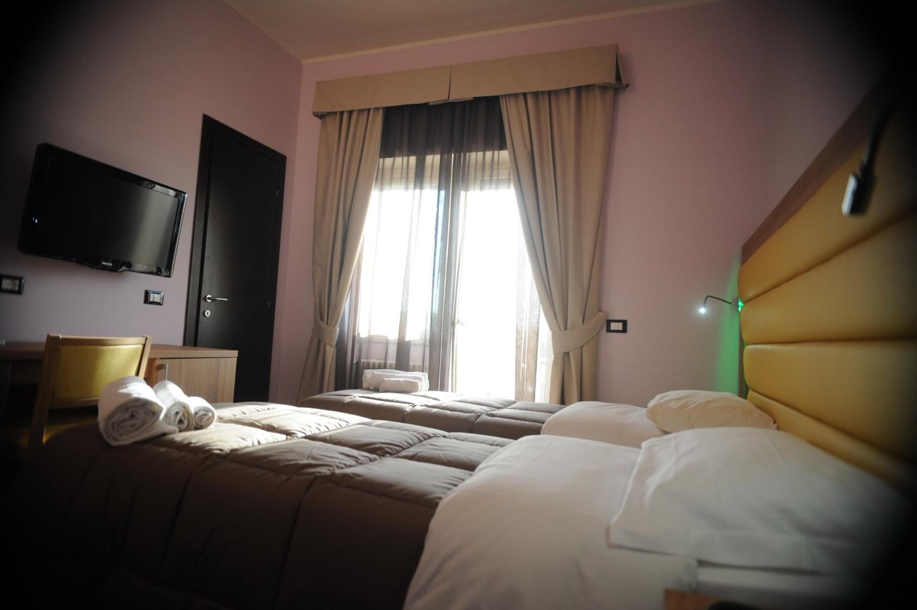 A hotel room with two beds, a television on the wall, and a window with curtains.