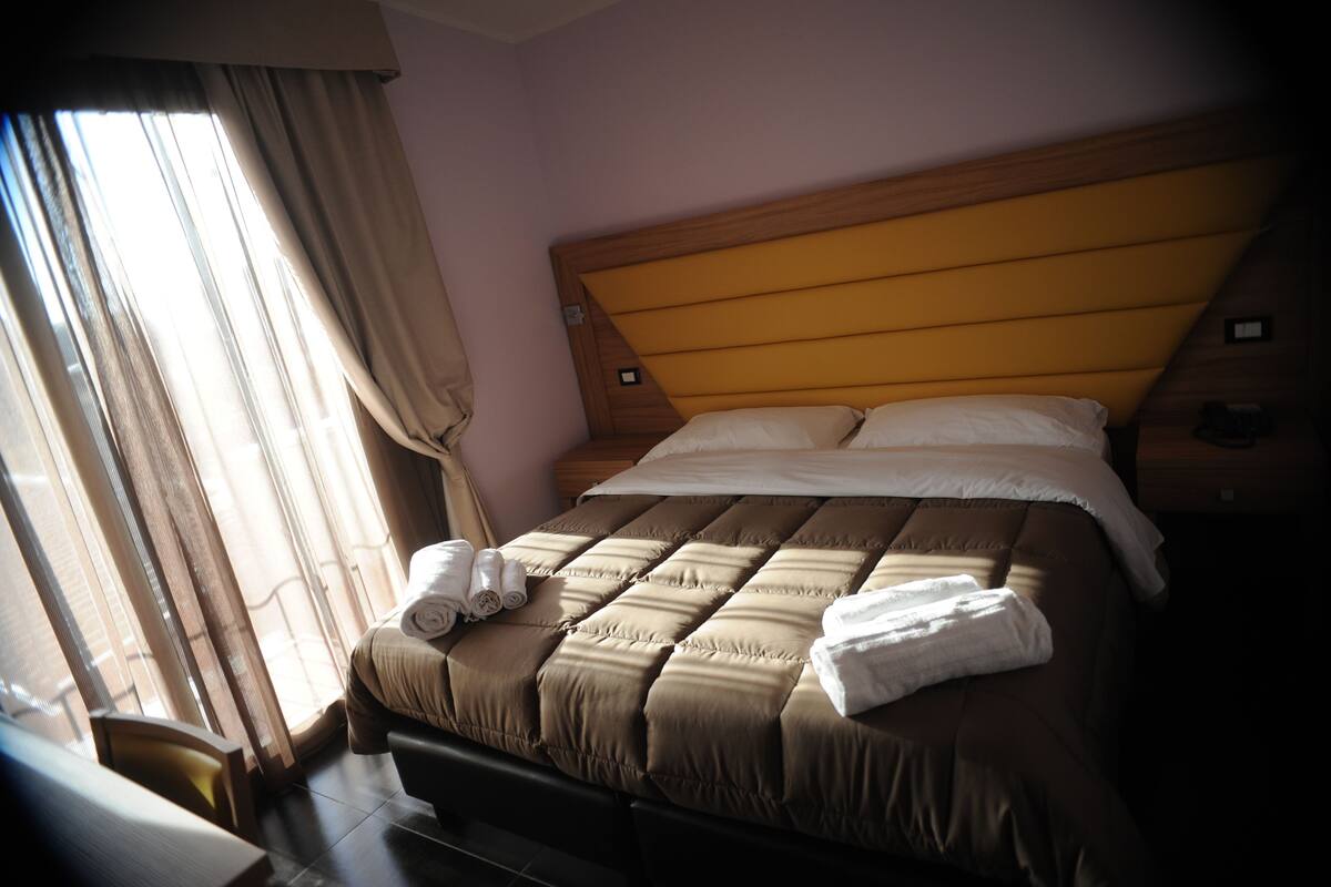 A hotel room with a large bed, a wooden headboard, and a window with curtains.