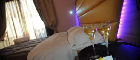 A hotel room with a bed, two champagne glasses on a table, and a flower on a napkin.