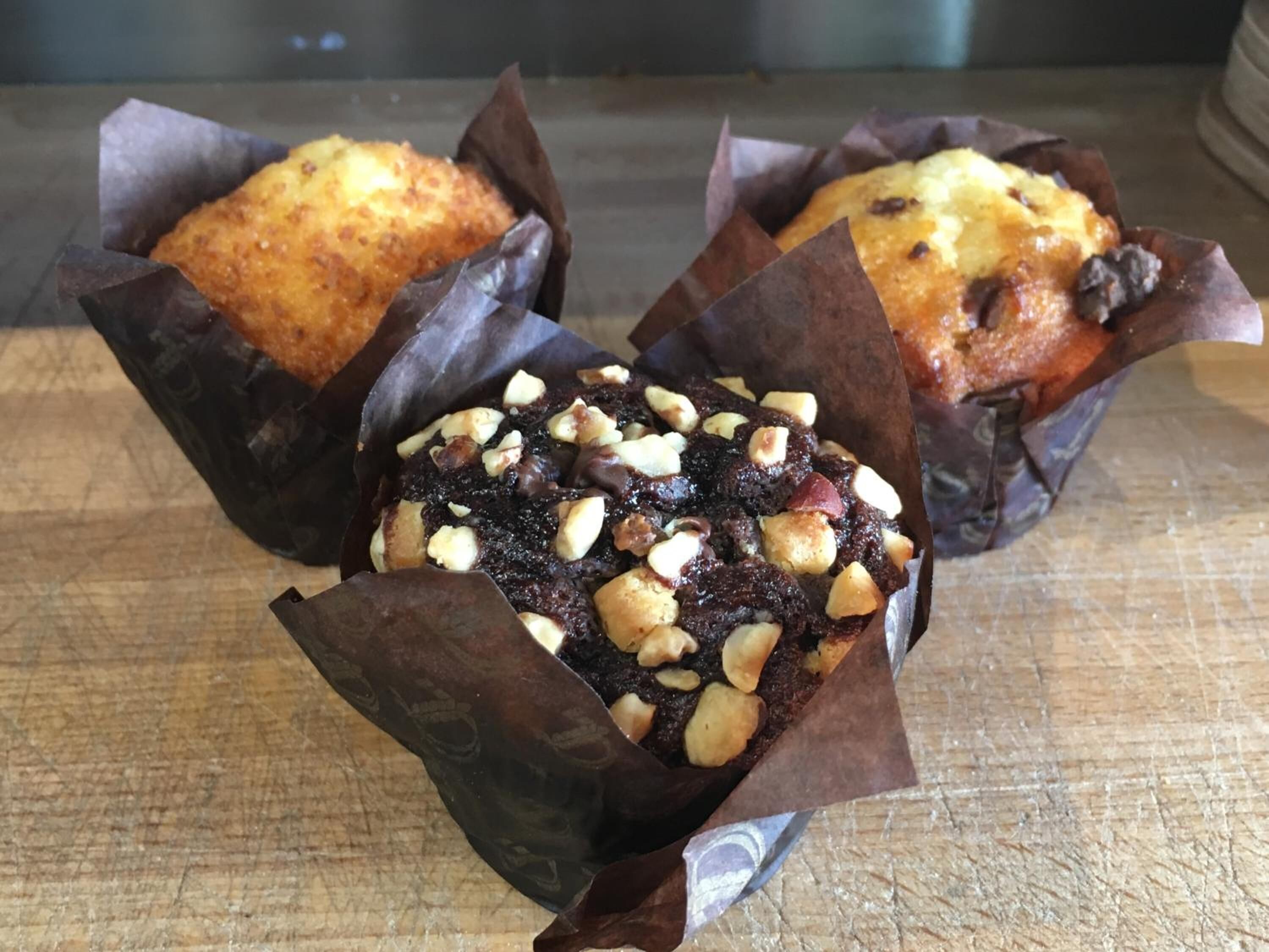 Three muffins in paper cups on a wooden surface.