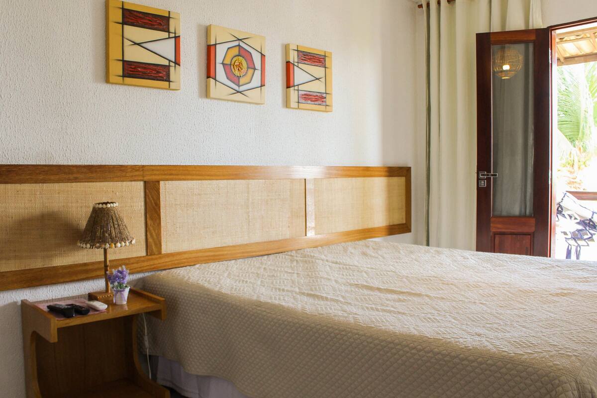 A neatly made bed with a wooden headboard, a bedside table with a lamp and remote control, and two abstract paintings on the wall.