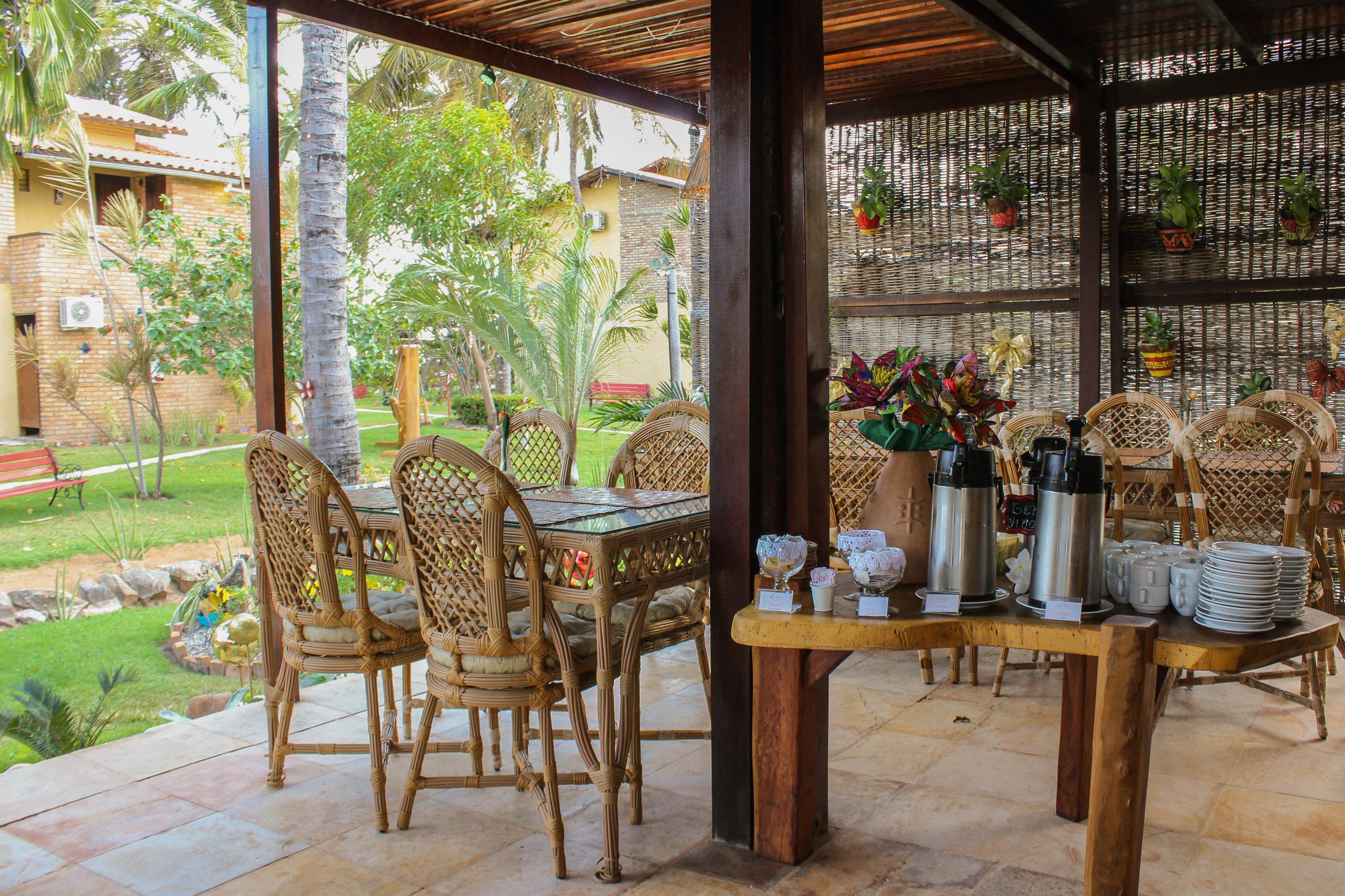Un espacio de comedor al aire libre con sillas de mimbre y una mesa dispuesta con platos, vasos y termos.