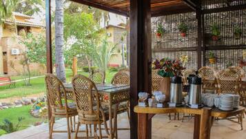 Un espacio de comedor al aire libre con sillas de mimbre y una mesa dispuesta con platos, vasos y termos.