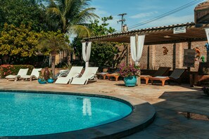 A swimming pool with lounge chairs and a covered area with a brick wall and palm trees. - Pousada do Paiva (Trairi)