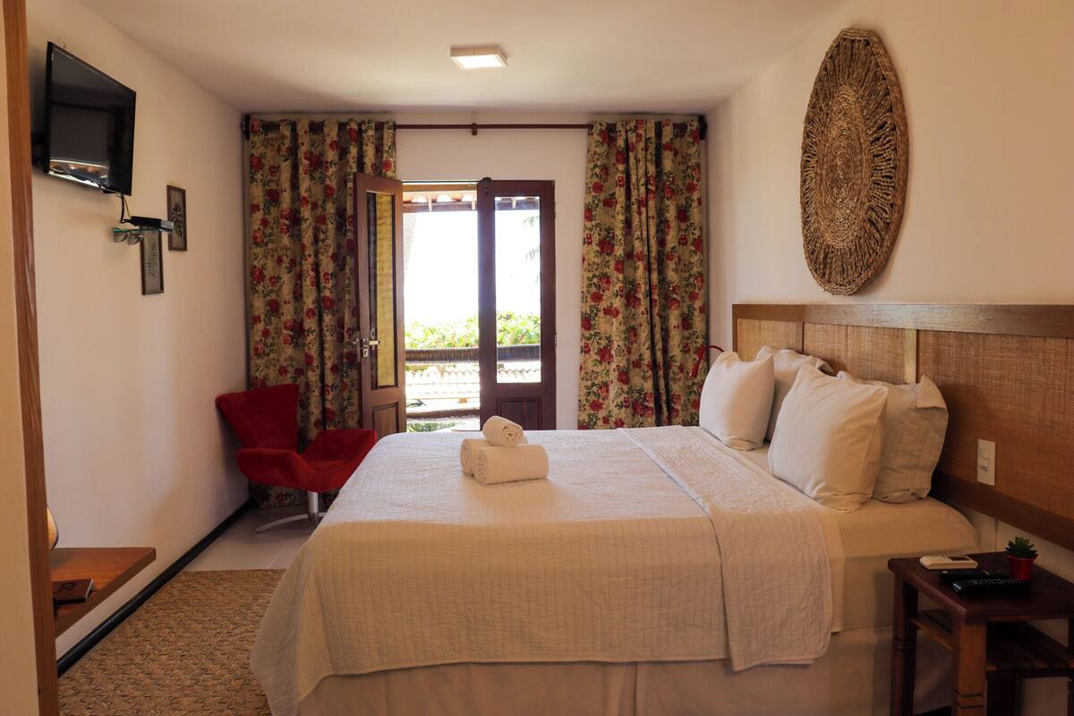 A hotel room with a bed, a red chair, a TV mounted on the wall, and a large woven wall decoration.