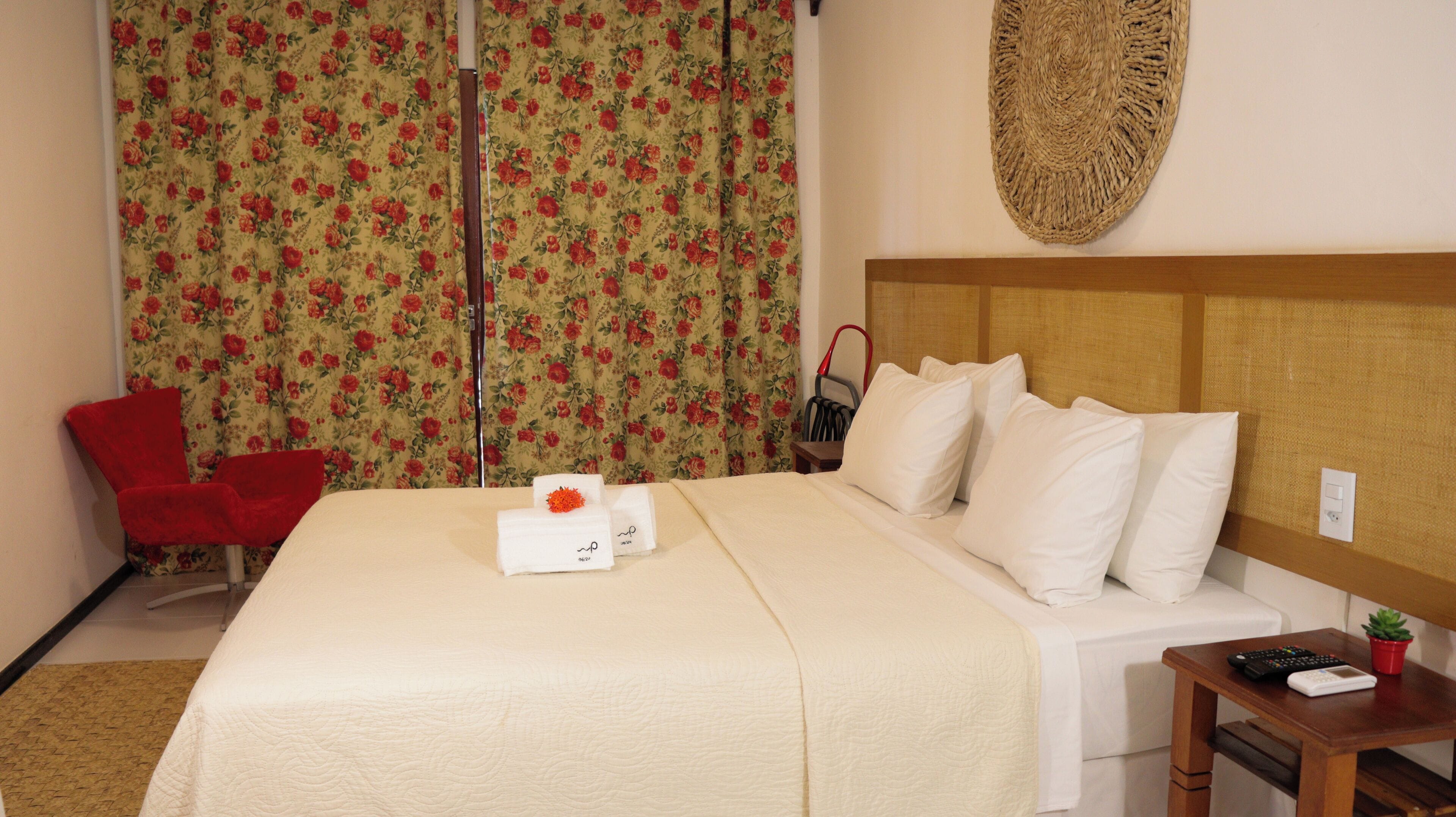 Ein Hotelzimmer mit einem Bett, einem roten Sessel, einem kleinen Tisch mit Fernbedienung und einem Wanddekor.