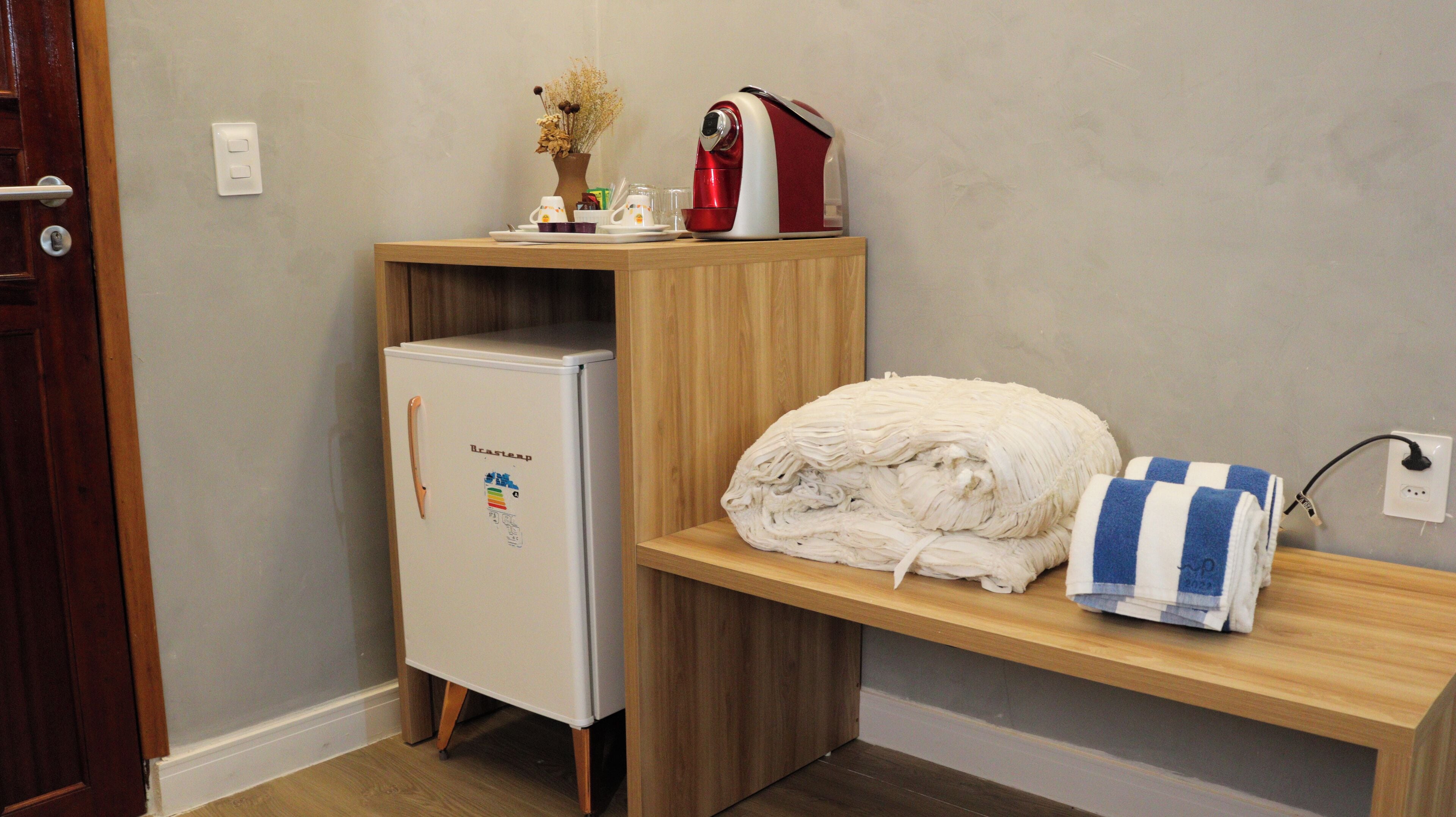 A compact kitchenette with a refrigerator, a microwave, and a small shelf with a towel and a kettle.