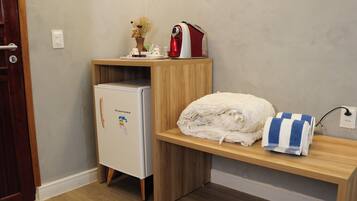 A compact kitchenette with a refrigerator, a microwave, and a small shelf with a towel and a kettle.