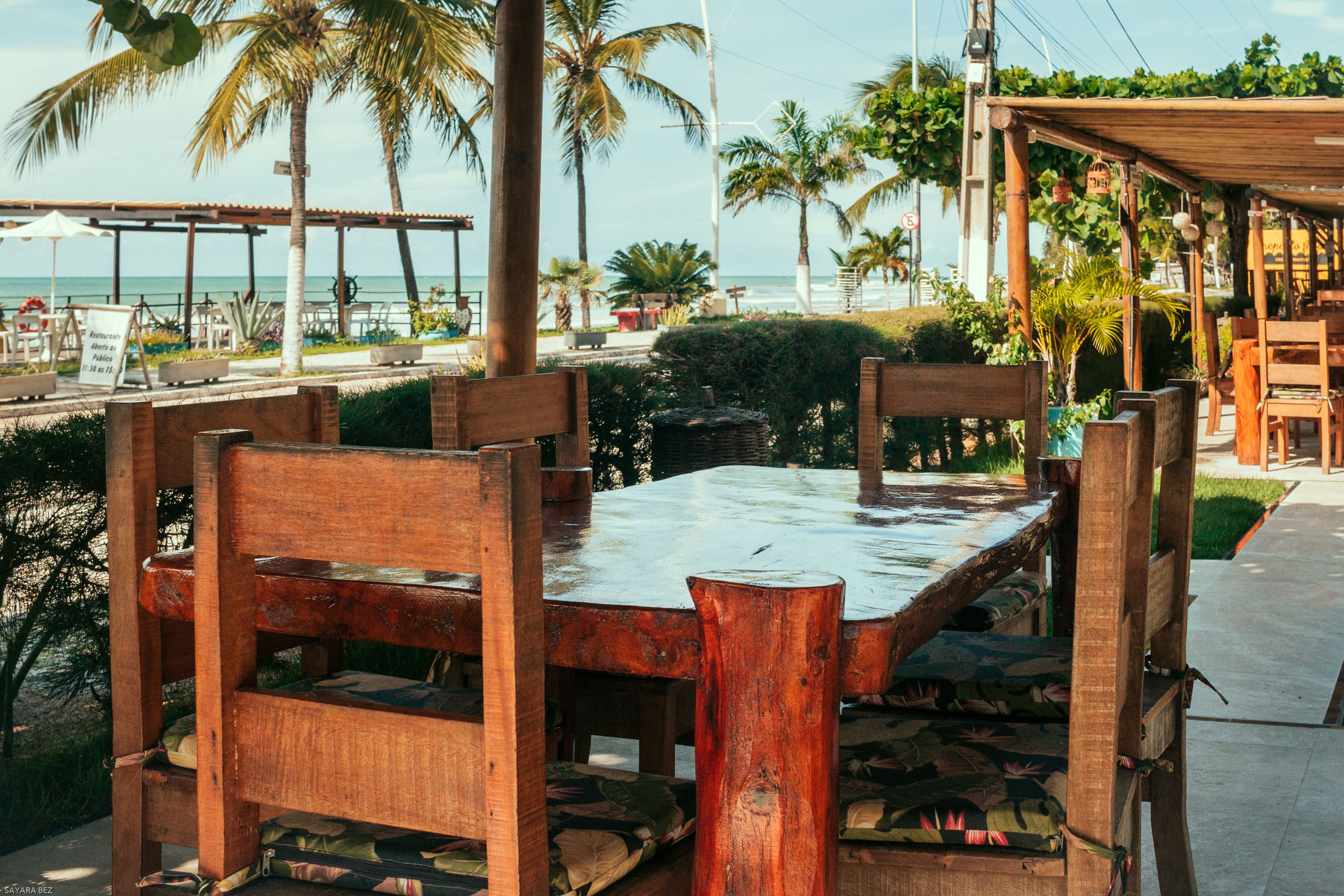 A wooden table with chairs, a view of the ocean, and palm trees.