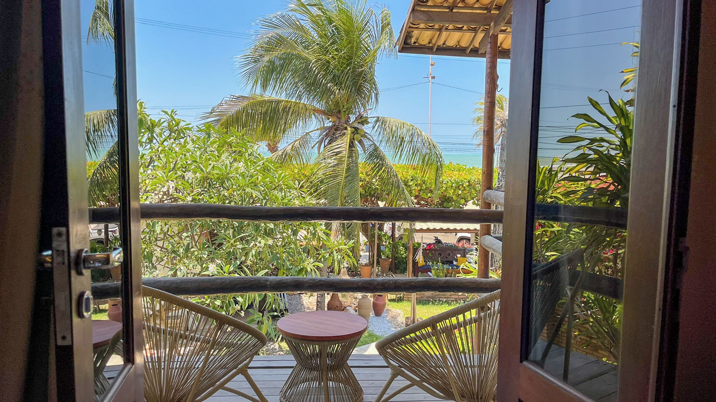 Un balcón con mobiliario de mimbre y vistas a una palmera y jardín.