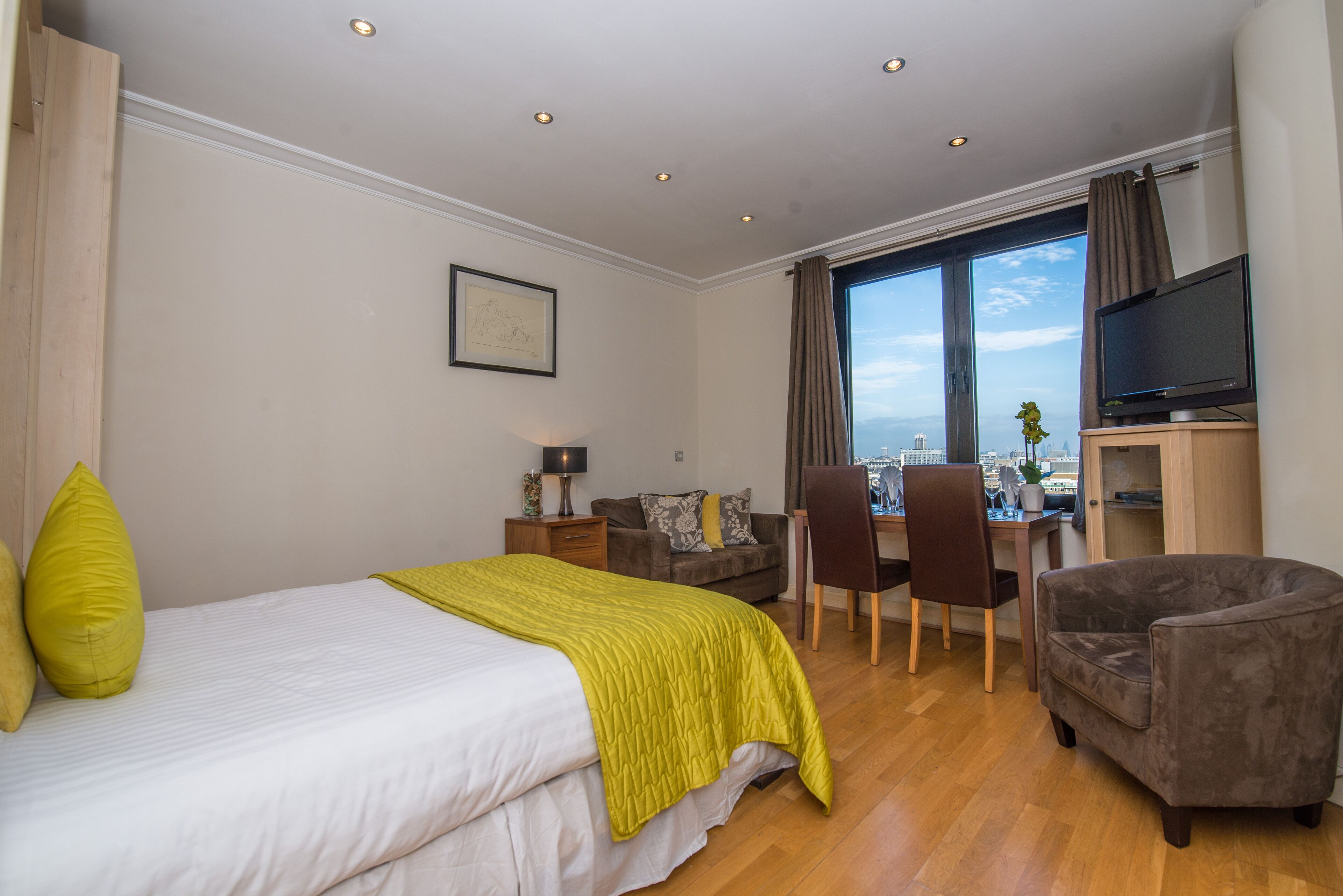 A hotel room with a bed, a desk, a chair, a TV, and a view of the city.