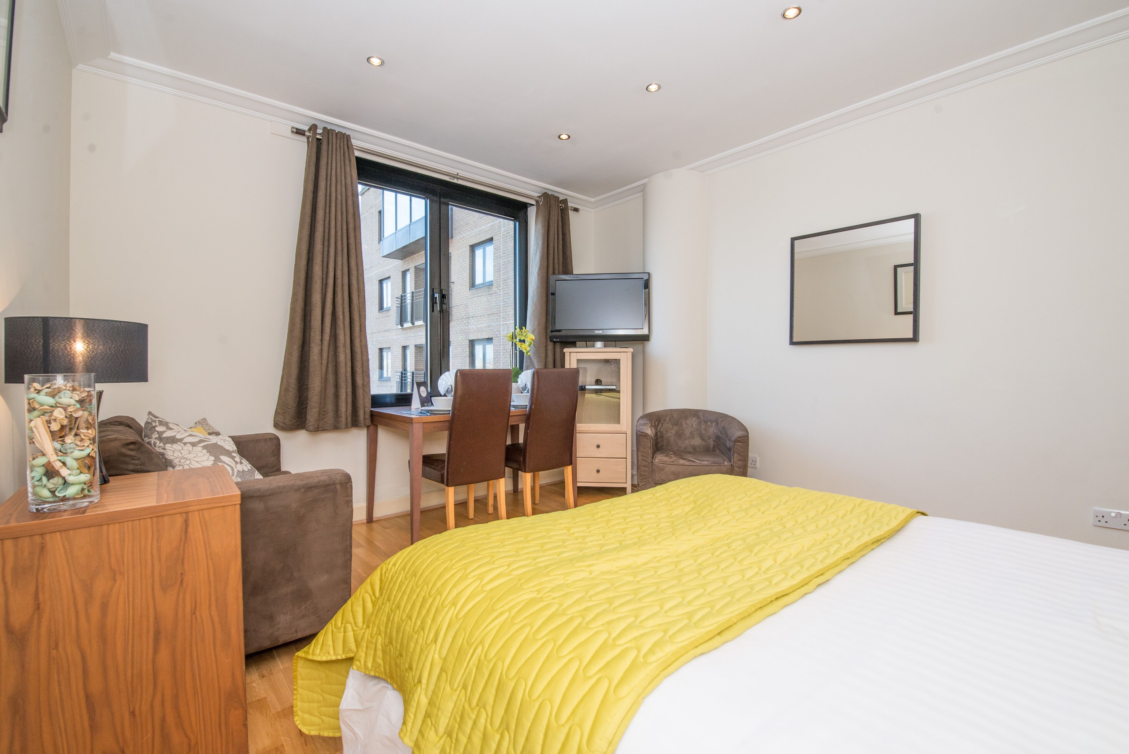 Een hotelkamer met een bed, een bureau met een computer, een stoel, een televisie en een raam met gordijnen.