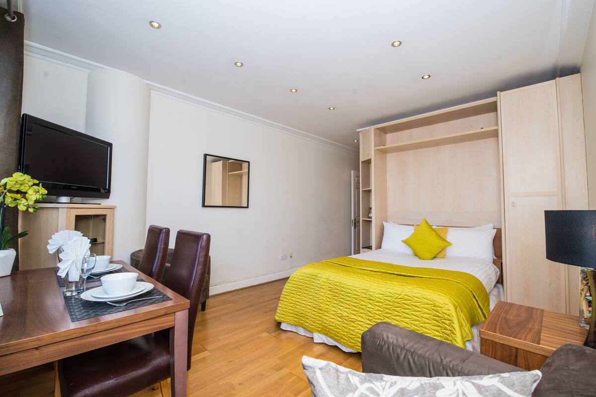 Ein Hotelzimmer mit Bett, Fernseher, Esstisch mit Stühlen und einem Holzschrank.