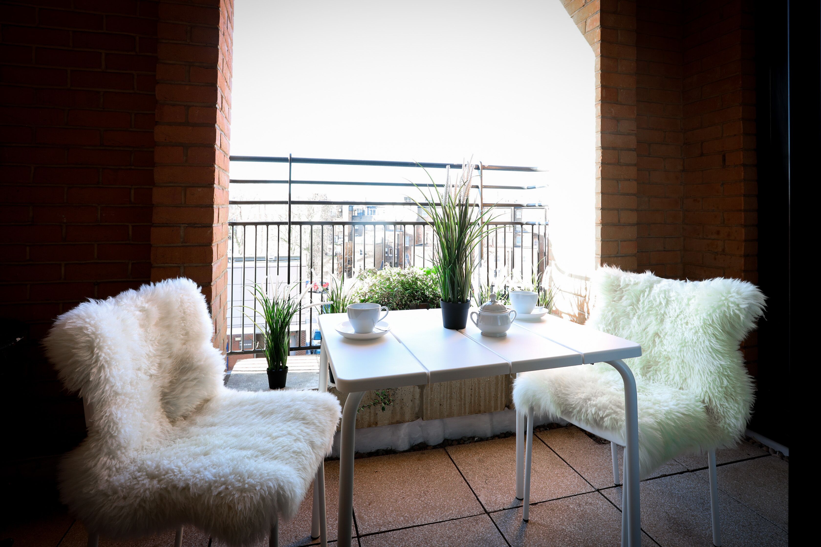 Un balcon avec deux fauteuils blancs à l’assise moelleuse, une table blanche et une plante en pot.