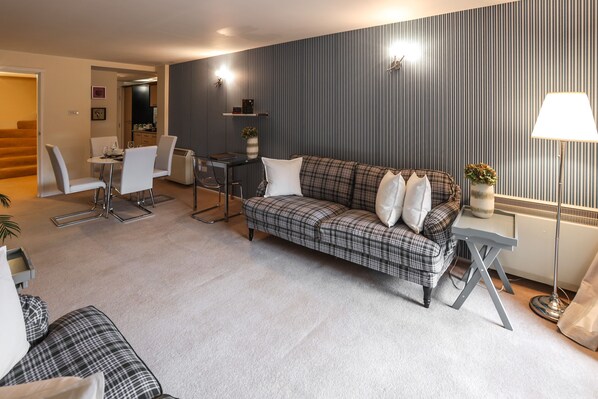 A modern living room with a plaid sofa, a dining table with chairs, and a small side table with a lamp.