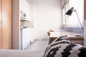 Ett modernt rum med en säng, ett skrivbord, en stol, en lampa, en mikrovågsugn och ett element.
