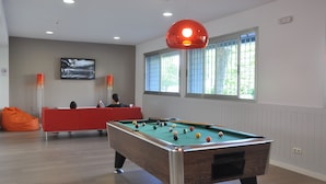 A pool table in a room with a red sofa, a television on the wall, and a window with blinds. - Residencia Universitaria Resa Tomás Alfaro Fournier - Centro Adscrito a REAJ - Campus Accomodation (Vitoria-Gasteiz)
