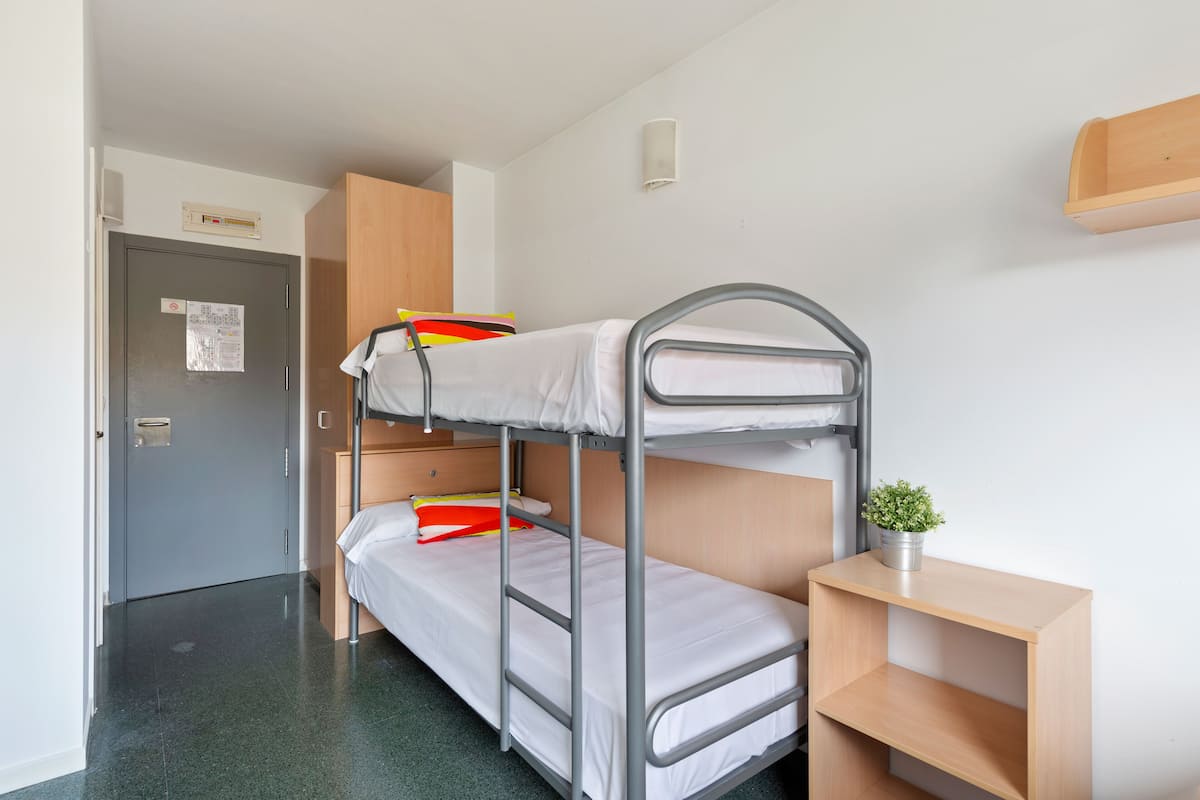 Une chambre avec un lit superposé, une armoire en bois, un petit bureau avec une plante et une porte sur laquelle est affiché un avis.