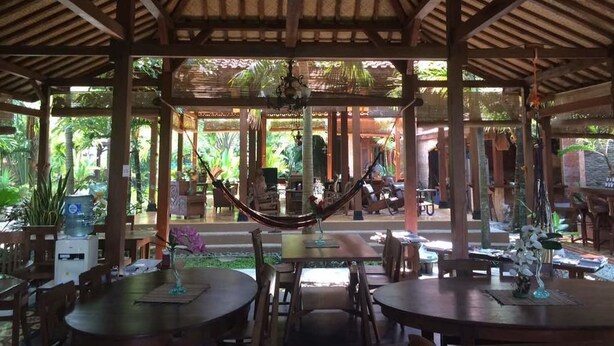 Un espacio al aire libre con mesas y sillas de madera, una hamaca y vistas de la vegetación circundante.
