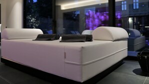 A modern living room with a white sofa, a large window, and a view of the cityscape. - B&B For 2 - Wellness For 2 (Bruges)