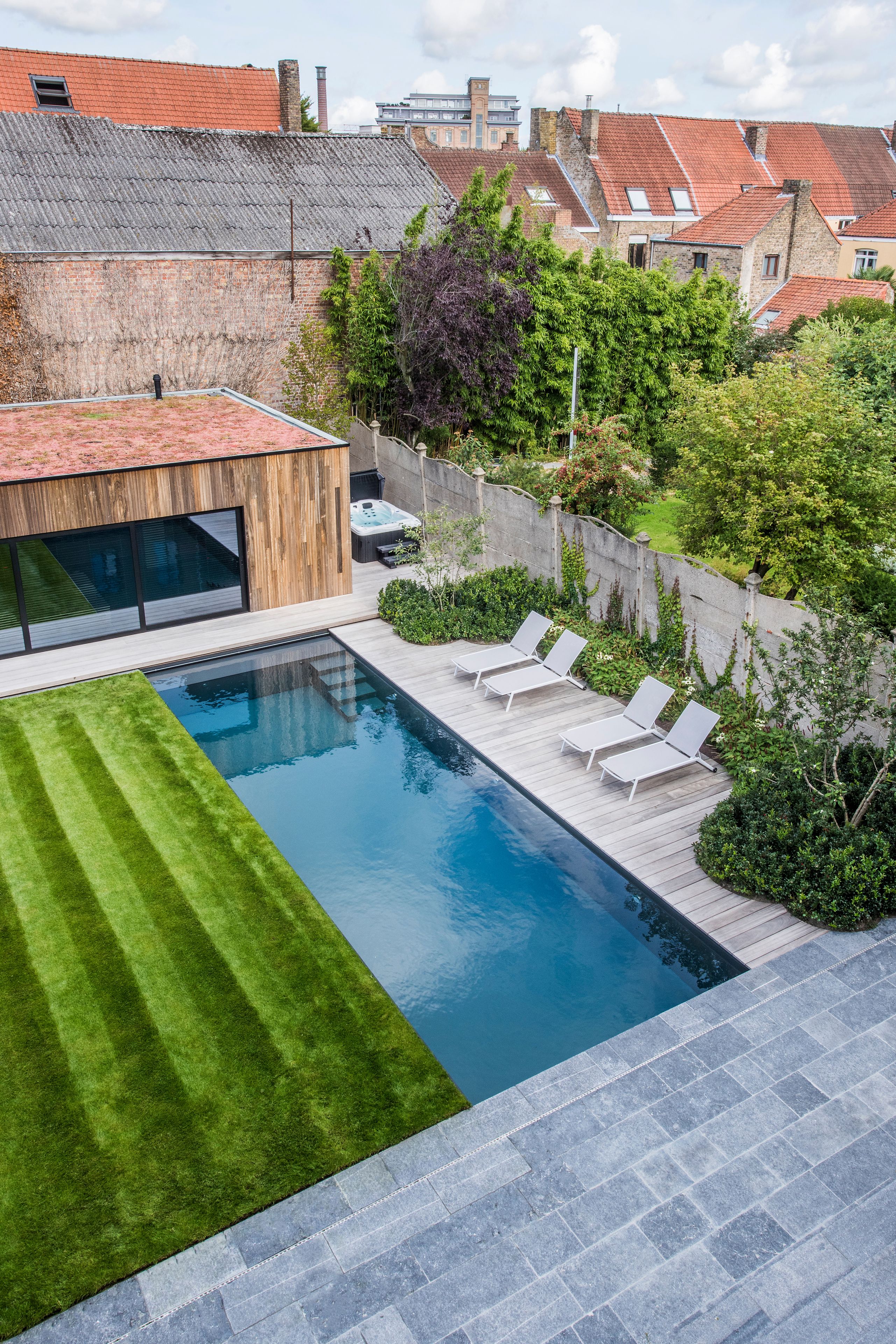 A modern outdoor pool area with a wooden deck, lounge chairs, and a well-maintained lawn.