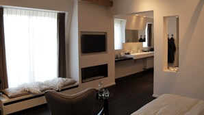 A modern hotel room with a sofa, a TV, a mirror, and a bathroom with a sink and mirror. - B&B For 2 - Wellness For 2 (Bruges)