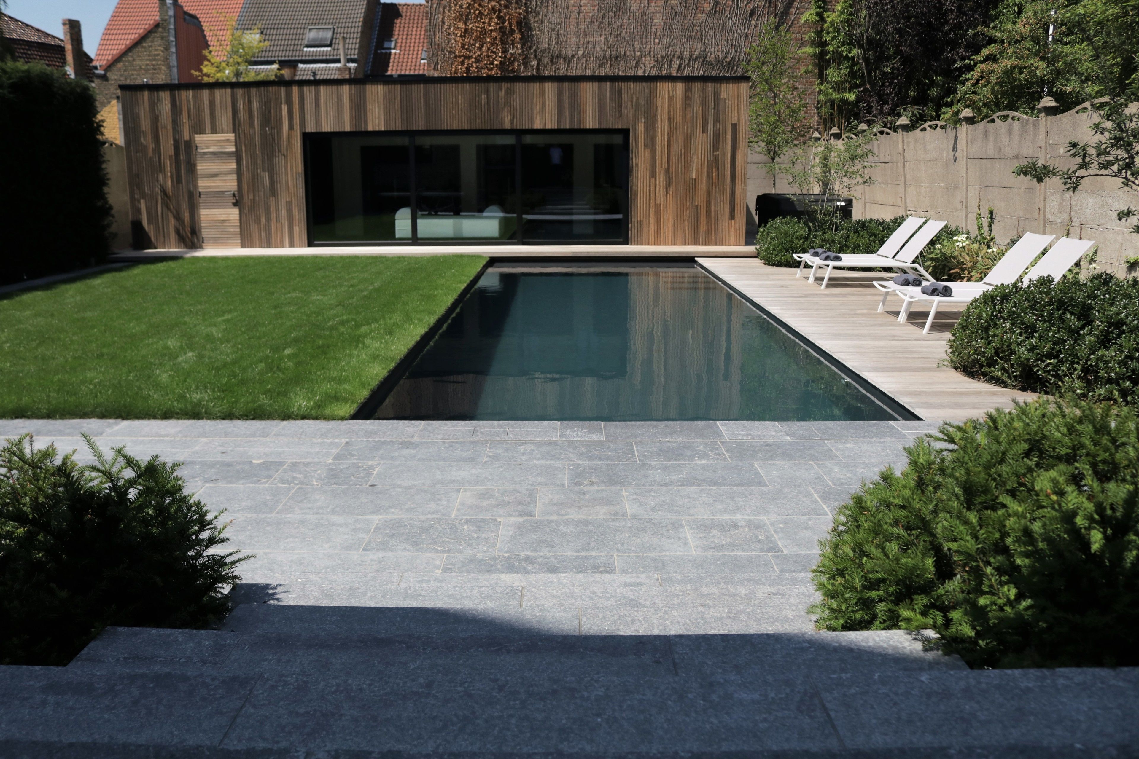 A modern house with a swimming pool, a wooden exterior, and a patio with lounge chairs.