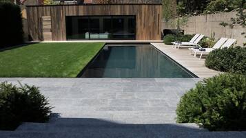 A modern house with a swimming pool, a wooden exterior, and a patio with lounge chairs.