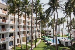 A multi-story hotel with balconies, a swimming pool, and palm trees.