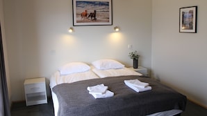 Een hotelkamer met een groot bed, twee nachtkastjes, een bijzettafeltje en een ingelijst schilderij aan de muur.