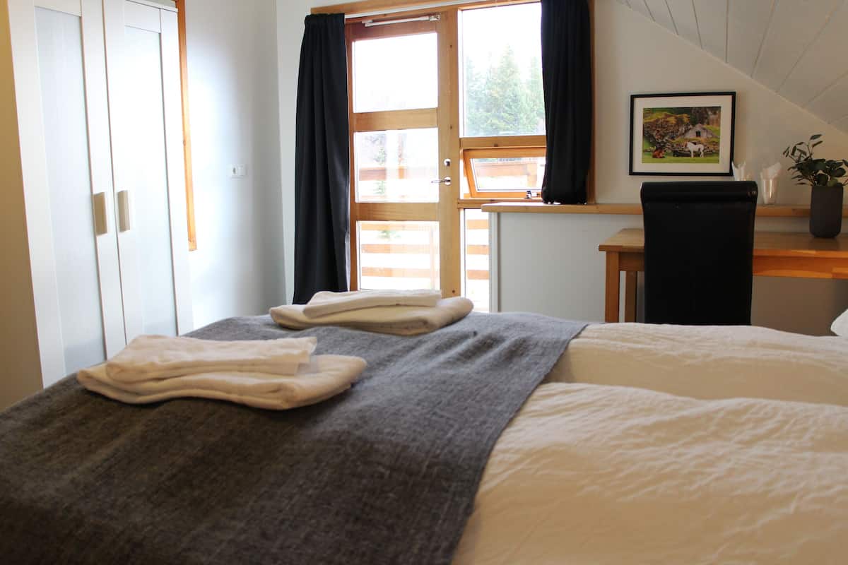 A bedroom with a bed, a desk, a chair, and a window with curtains.