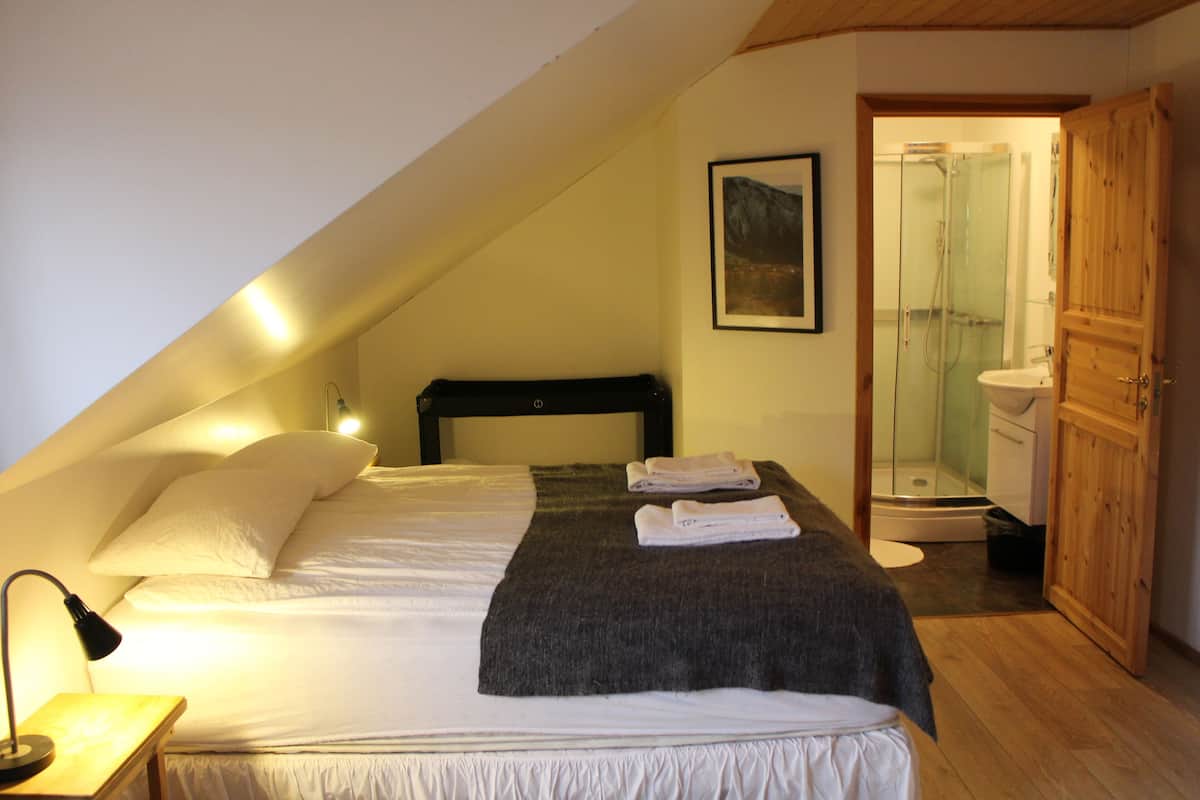 A bedroom with a bed, a bedside lamp, a wooden door, and a bathroom visible through an open door.