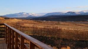 Een houten terras met uitzicht op een bergachtig landschap, met besneeuwde toppen en een heldere lucht.