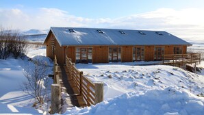 Een houten lodge met een metalen dak, een houten terras en een besneeerd landschap.