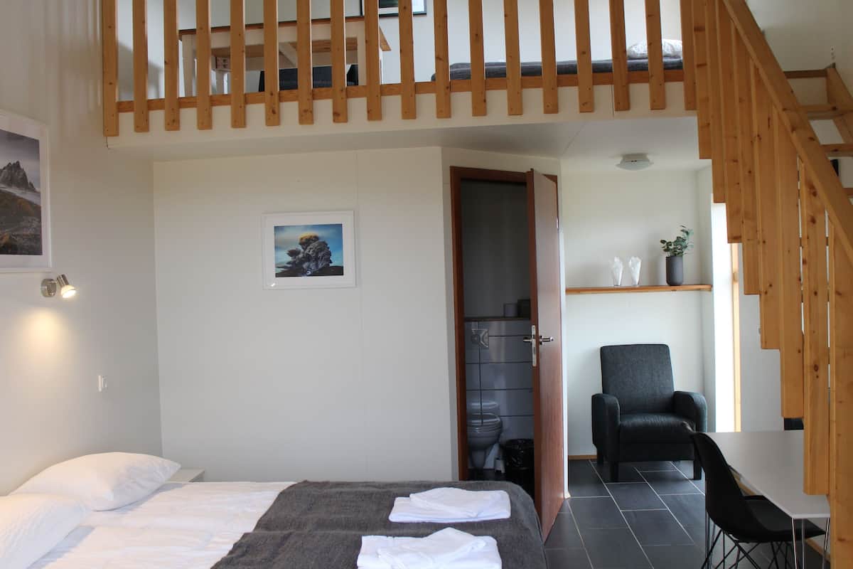 A bedroom with a bed, a chair, a desk, and a staircase.