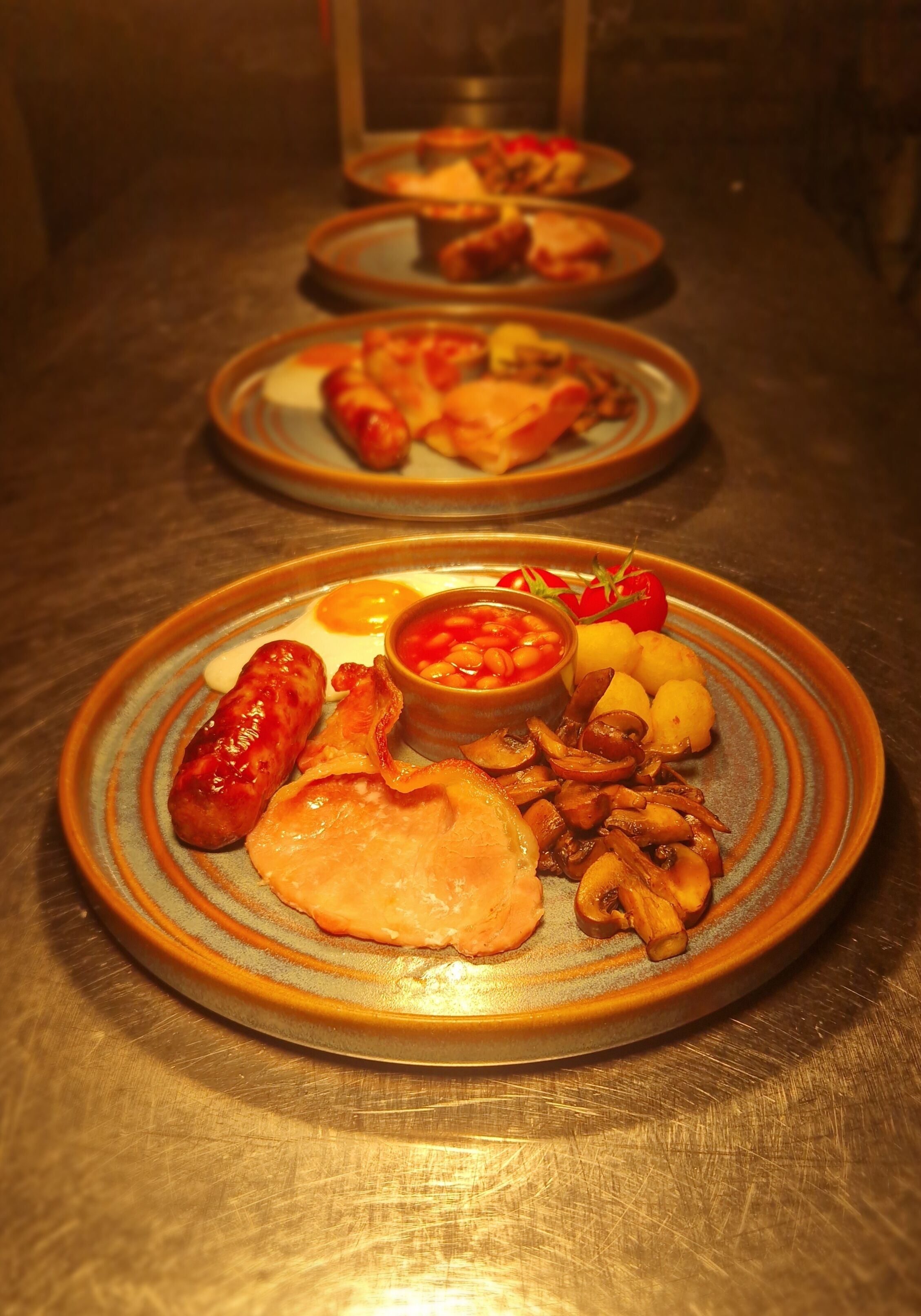 Een tafel met borden eten, waaronder worstjes, eieren, champignons en tomaten.