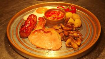 Een tafel met borden eten, waaronder worstjes, eieren, champignons en tomaten.