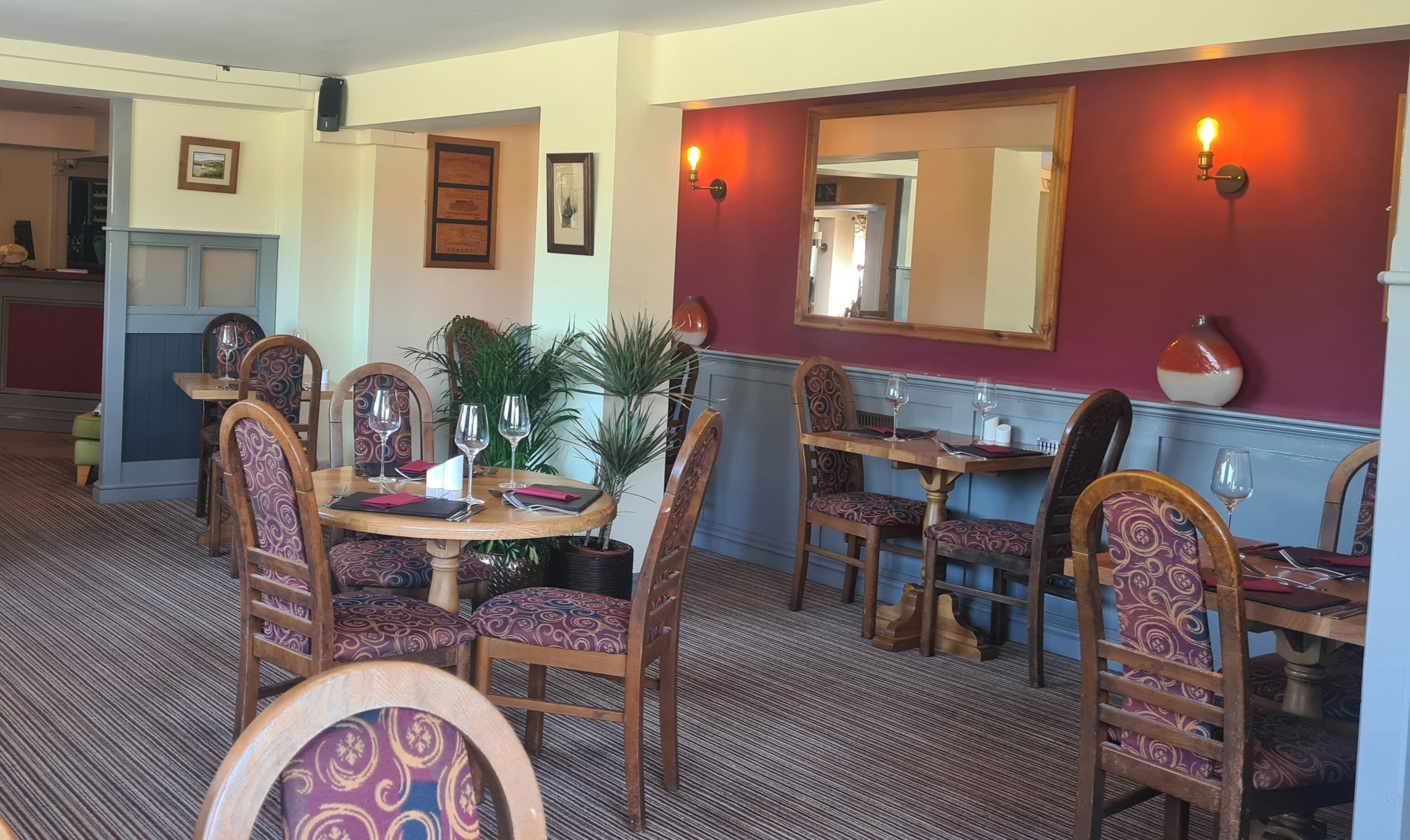 Un coin repas avec des tables et des chaises en bois, une plante en pot et des tableaux encadrés accrochés aux murs.