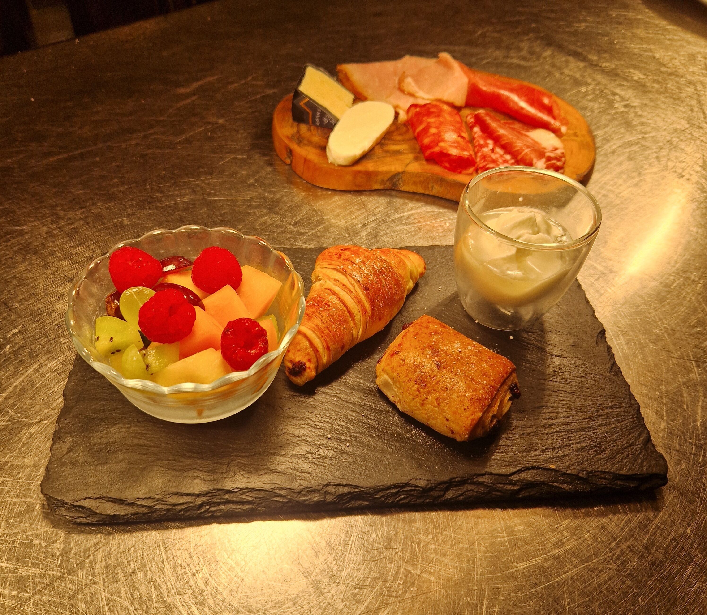 Un plat amb fruita, formatge i un croissant sobre una taula de pedra.