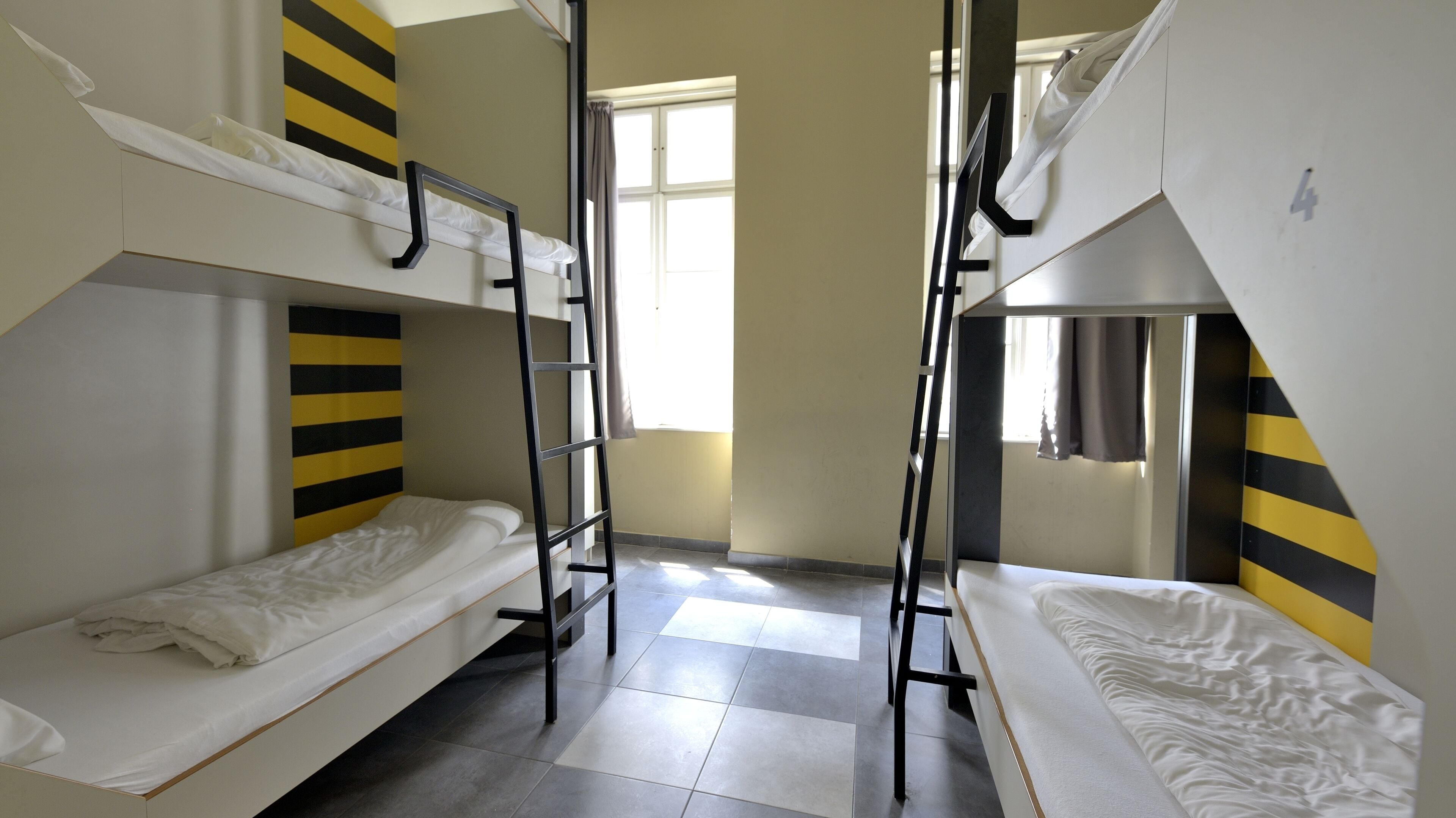 A dormitory room with bunk beds, a window, and a tiled floor.