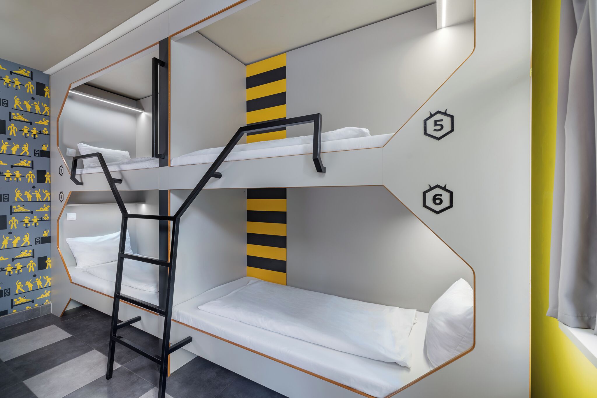 Dormitorio con literas, una escalera, literas numeradas y un adorno de pared a rayas.